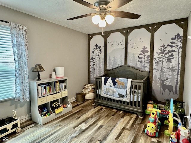 bedroom with hardwood / wood-style floors, ceiling fan, a textured ceiling, and a nursery area