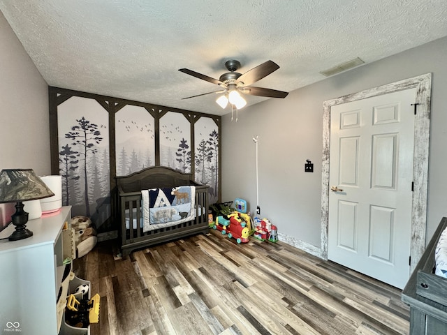 bedroom with hardwood / wood-style floors, a textured ceiling, a nursery area, and ceiling fan