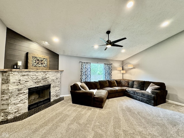 carpeted living room with a textured ceiling, vaulted ceiling, ceiling fan, and a stone fireplace