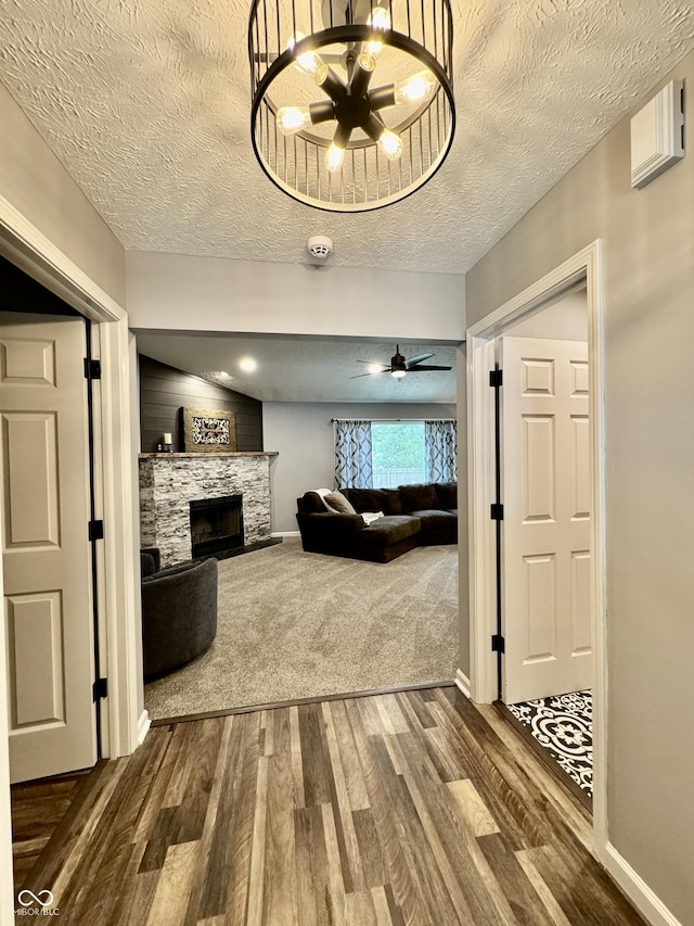 living room with a textured ceiling, ceiling fan with notable chandelier, wood-type flooring, and a fireplace