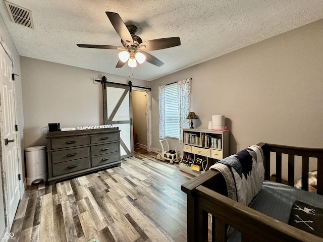 bedroom with a barn door, ceiling fan, light hardwood / wood-style flooring, and a textured ceiling