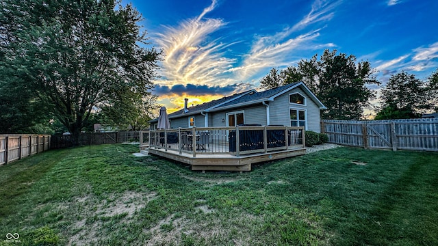 back house at dusk featuring a wooden deck and a lawn