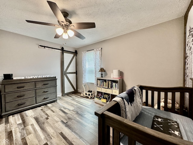 bedroom with a textured ceiling, a barn door, light hardwood / wood-style flooring, and ceiling fan