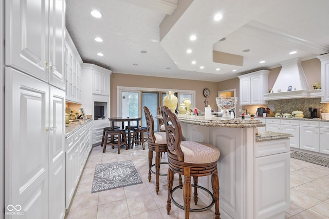 kitchen with white cabinets, light stone counters, decorative backsplash, light tile patterned flooring, and custom range hood