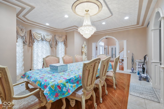 tiled dining room featuring a tray ceiling, a textured ceiling, ornamental molding, and an inviting chandelier