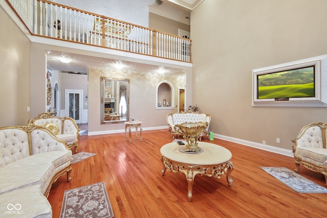 living room with wood-type flooring, crown molding, and a towering ceiling