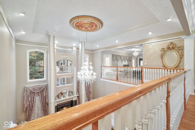 hallway featuring a notable chandelier, decorative columns, a textured ceiling, hardwood / wood-style floors, and a raised ceiling