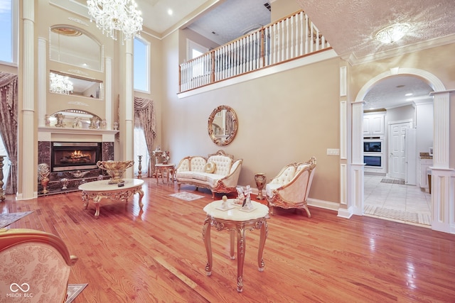 living room featuring a notable chandelier, a high ceiling, light wood-type flooring, a premium fireplace, and a textured ceiling