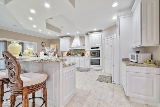 kitchen with white appliances, white cabinets, light stone counters, light tile patterned floors, and custom exhaust hood