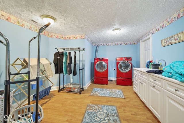 laundry area with light hardwood / wood-style floors, cabinets, washing machine and dryer, and a textured ceiling