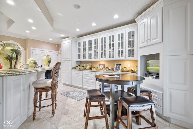 kitchen featuring ornamental molding, light tile patterned floors, white cabinets, and a kitchen breakfast bar