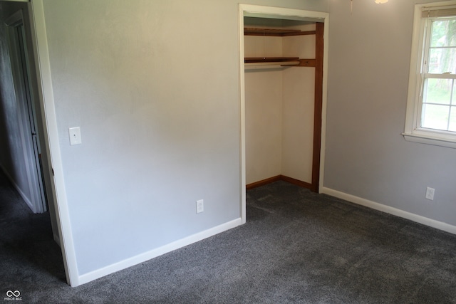 unfurnished bedroom featuring a closet, multiple windows, and dark colored carpet