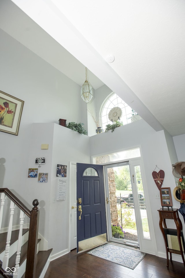 foyer entrance with dark wood-type flooring, an inviting chandelier, and a towering ceiling