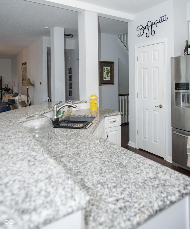 kitchen with light stone counters, dark hardwood / wood-style floors, stainless steel refrigerator with ice dispenser, sink, and white cabinetry