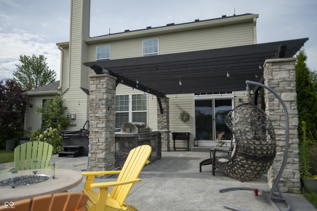 rear view of property featuring an outdoor fire pit, a hot tub, a patio area, exterior kitchen, and a pergola