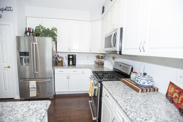 kitchen with stainless steel appliances, white cabinets, light stone counters, and dark wood-type flooring