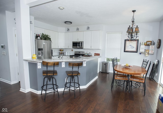 kitchen with stainless steel appliances, white cabinetry, a kitchen breakfast bar, kitchen peninsula, and dark hardwood / wood-style flooring