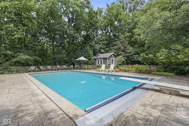 view of pool featuring an outdoor structure, a diving board, and a patio