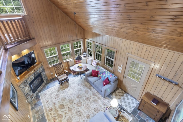 living room featuring a stone fireplace, a healthy amount of sunlight, wooden ceiling, and wooden walls