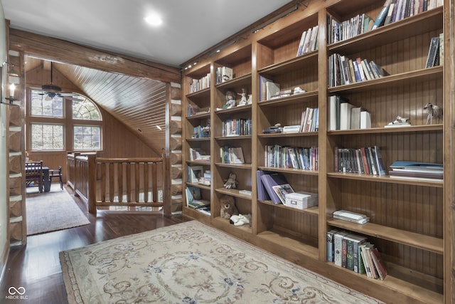 living area featuring lofted ceiling, dark wood-type flooring, wooden walls, and ceiling fan