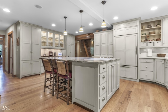 kitchen featuring a kitchen breakfast bar, hanging light fixtures, a center island, paneled built in fridge, and light hardwood / wood-style flooring