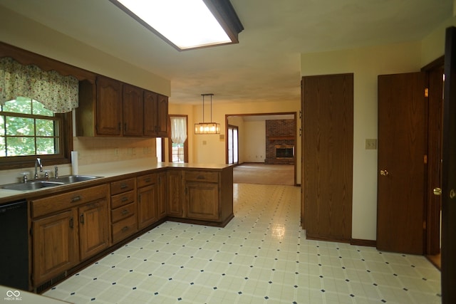 kitchen featuring sink, hanging light fixtures, black dishwasher, a fireplace, and kitchen peninsula