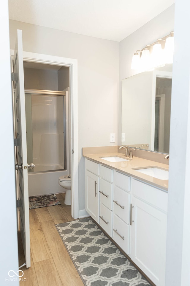 full bathroom with vanity, bath / shower combo with glass door, hardwood / wood-style flooring, and toilet