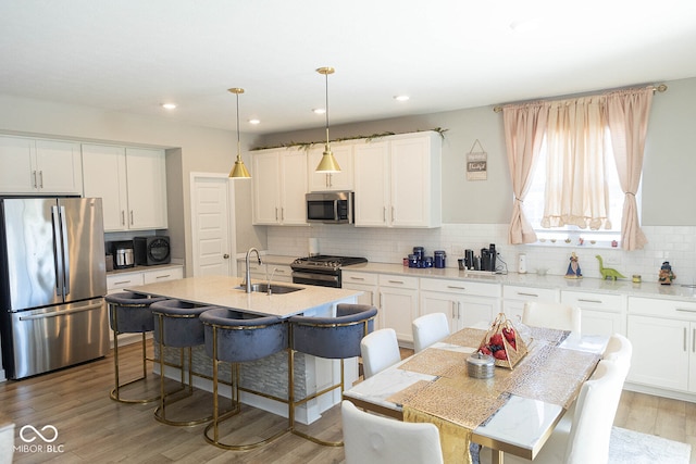 kitchen with appliances with stainless steel finishes, white cabinets, light wood-type flooring, decorative light fixtures, and sink