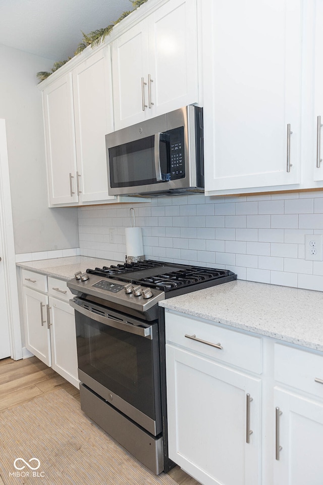 kitchen with light wood-type flooring, white cabinetry, backsplash, appliances with stainless steel finishes, and light stone countertops