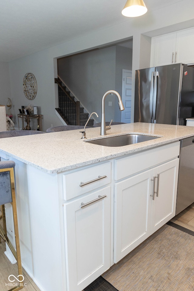 kitchen with light stone counters, sink, white cabinetry, appliances with stainless steel finishes, and light hardwood / wood-style floors