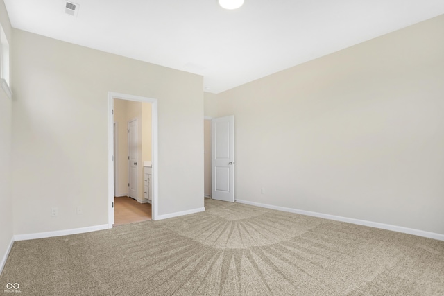 unfurnished bedroom featuring light carpet and ensuite bath