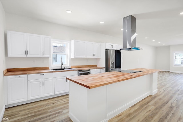 kitchen featuring appliances with stainless steel finishes, sink, white cabinets, butcher block countertops, and island range hood