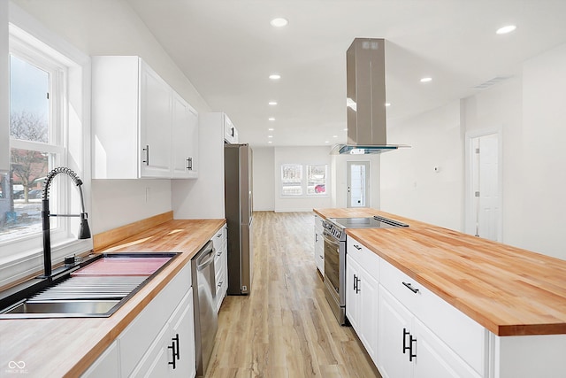 kitchen with sink, island range hood, butcher block counters, and stainless steel appliances