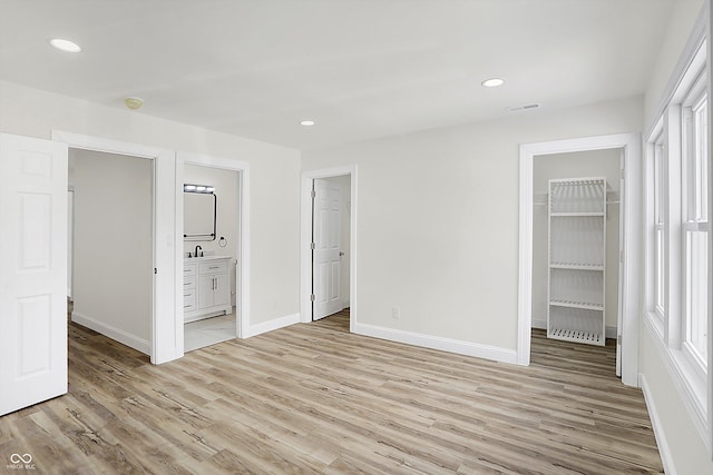 unfurnished bedroom with a walk in closet, ensuite bathroom, light hardwood / wood-style floors, and a closet