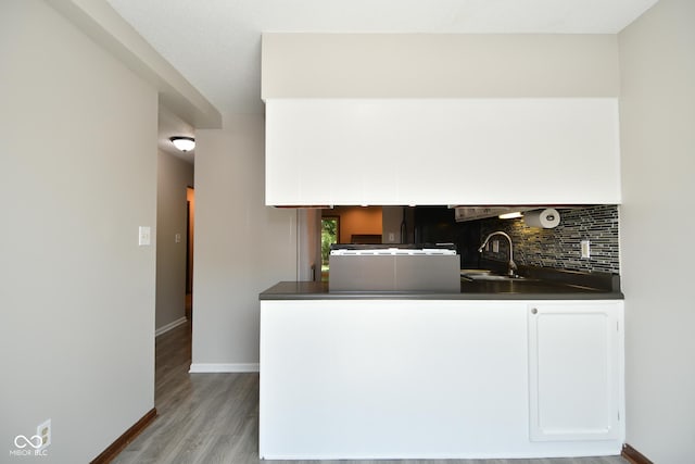 kitchen with white cabinetry, sink, backsplash, kitchen peninsula, and light hardwood / wood-style flooring