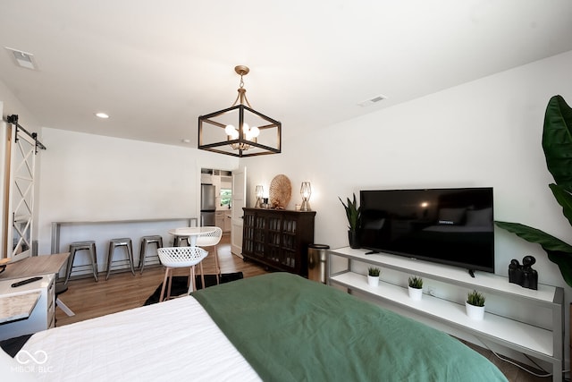 bedroom featuring hardwood / wood-style floors, an inviting chandelier, stainless steel fridge, and a barn door