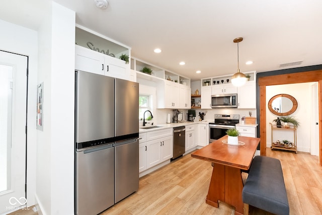 kitchen with appliances with stainless steel finishes, light hardwood / wood-style flooring, white cabinets, and decorative light fixtures