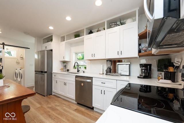 kitchen featuring stainless steel appliances, white cabinets, washer and clothes dryer, sink, and light hardwood / wood-style floors