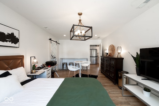 bedroom featuring stainless steel fridge, a notable chandelier, a barn door, and hardwood / wood-style flooring