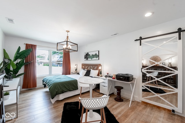 bedroom with an inviting chandelier, a barn door, and wood-type flooring