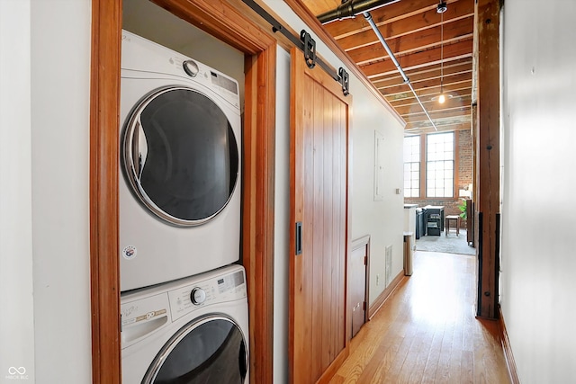 laundry room featuring light hardwood / wood-style floors, stacked washer and dryer, and a barn door