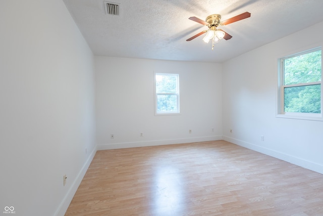 unfurnished room featuring baseboards, light wood-style flooring, visible vents, and a textured ceiling