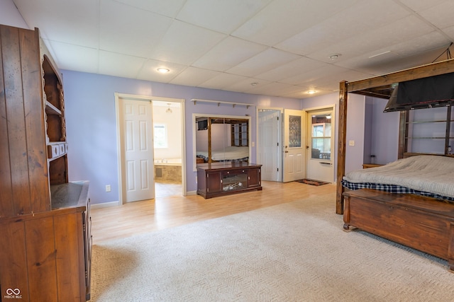 carpeted bedroom with wood finished floors, a drop ceiling, baseboards, and ensuite bathroom