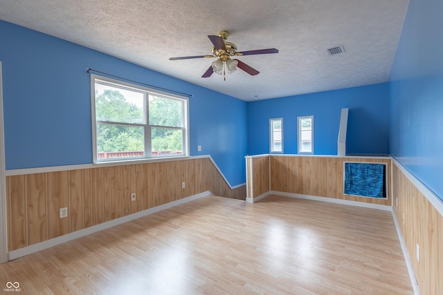 empty room featuring a textured ceiling, visible vents, a wealth of natural light, and wainscoting