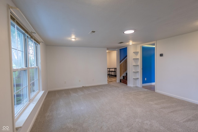 spare room with built in shelves, visible vents, baseboards, stairway, and carpet