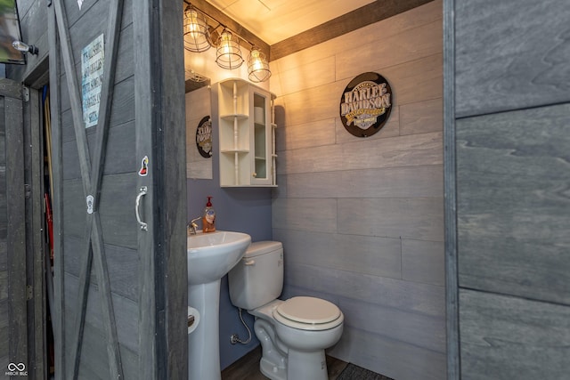 bathroom featuring toilet, wooden walls, and a sink