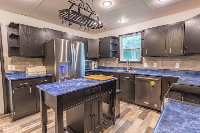 kitchen with open shelves, backsplash, appliances with stainless steel finishes, light wood-style floors, and a sink