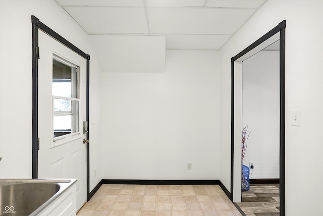 empty room featuring light floors, a drop ceiling, a sink, and baseboards