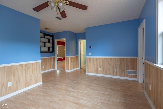 spare room featuring a ceiling fan, a wainscoted wall, visible vents, and wood finished floors