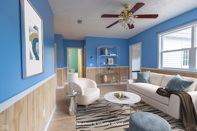 living area featuring visible vents, light wood-style floors, wainscoting, a textured ceiling, and wood walls